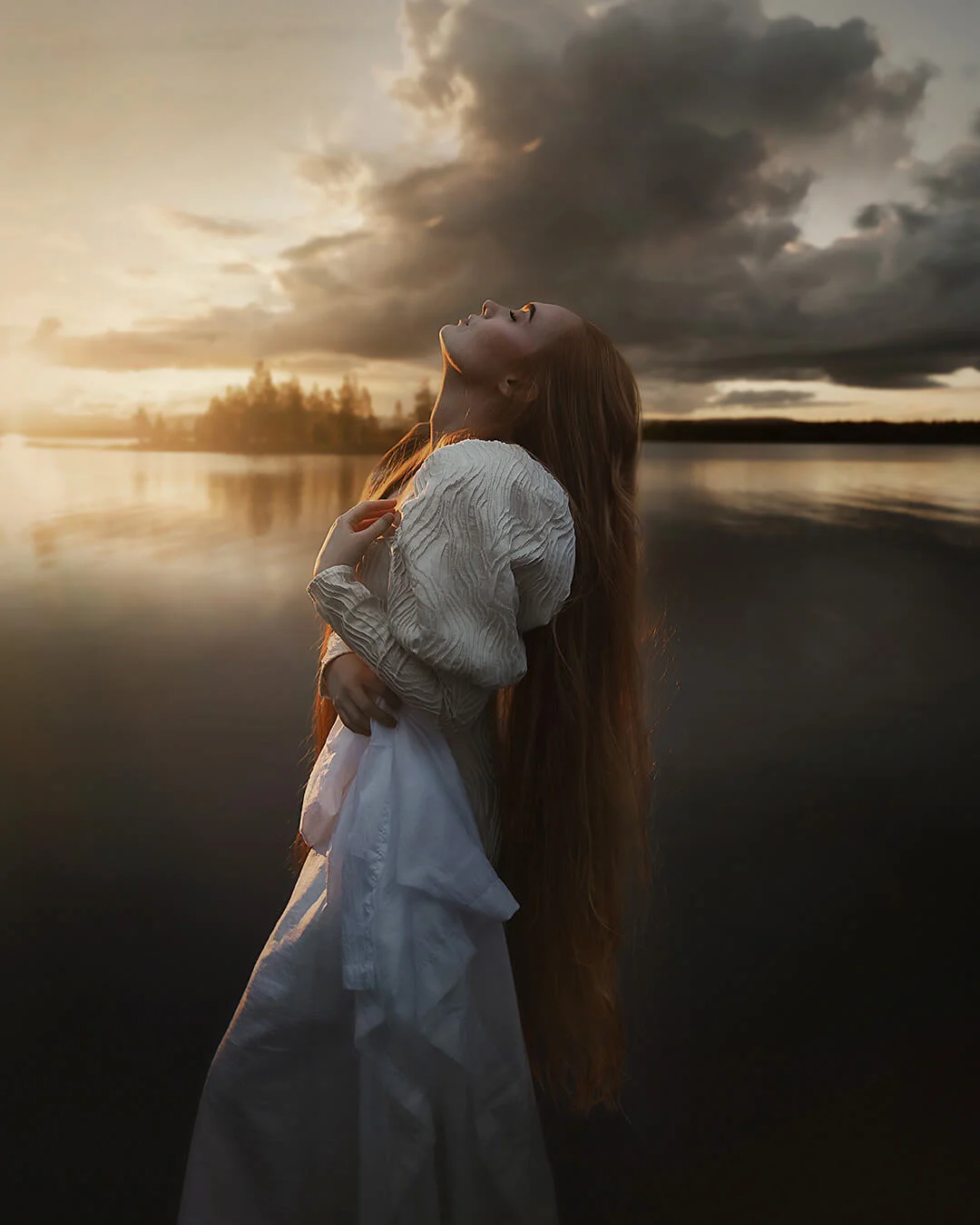 Porträttfotografering - en kvinna (Natali Skoglund) med rött långt hår står vid vattnet och njuter av solen. Portrait photography - a woman (Natali Skoglund) with long red hair stands by the water and enjoys the sun.