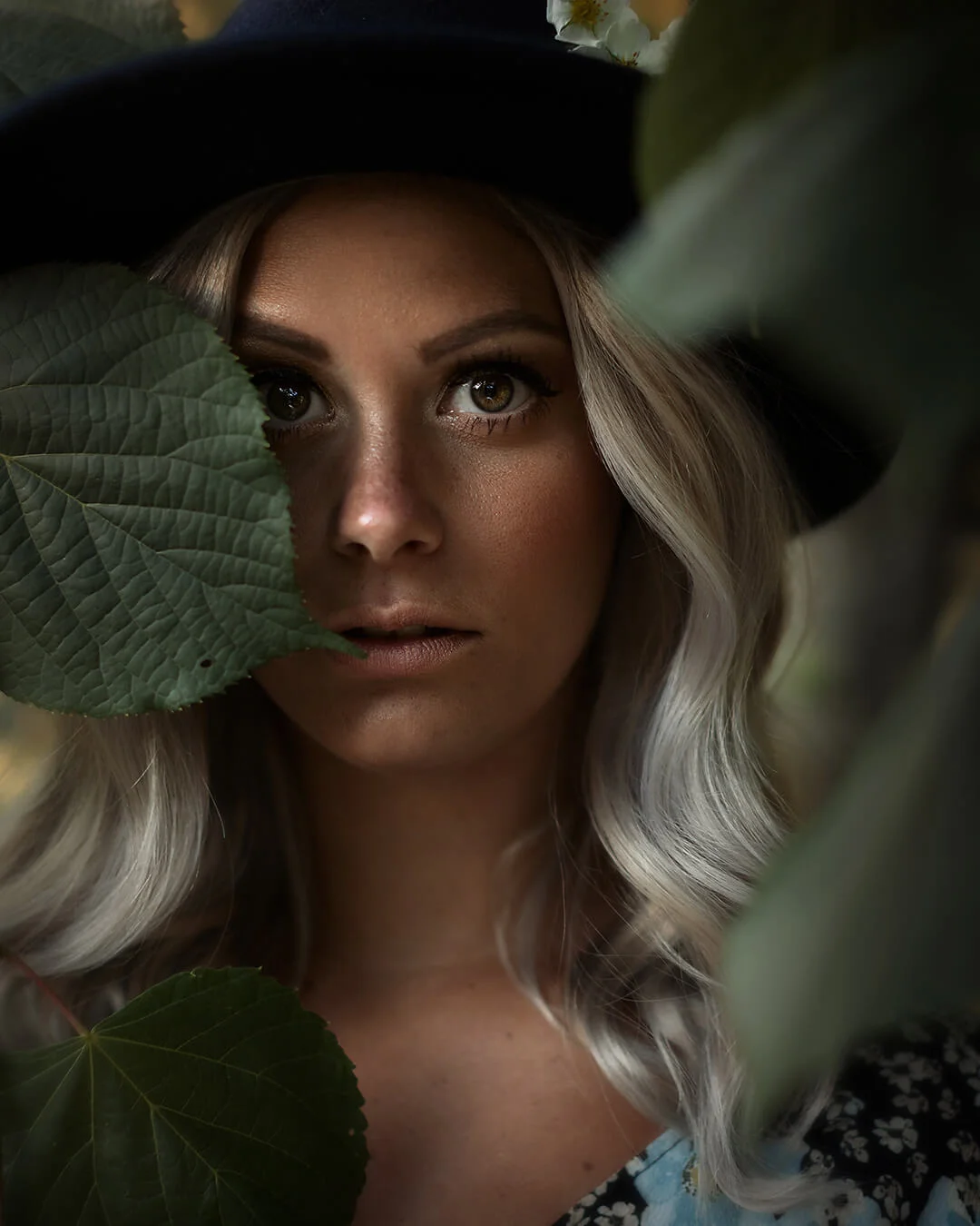 Porträttfotografering - kvinna med silverblondt hår (Rebecca Zufic) står bland gröna blad. Stora vackra ögon. Portrait photography - woman with silver blonde hair (Rebecca Zufic) standing among green leaves. Big beautiful eyes.