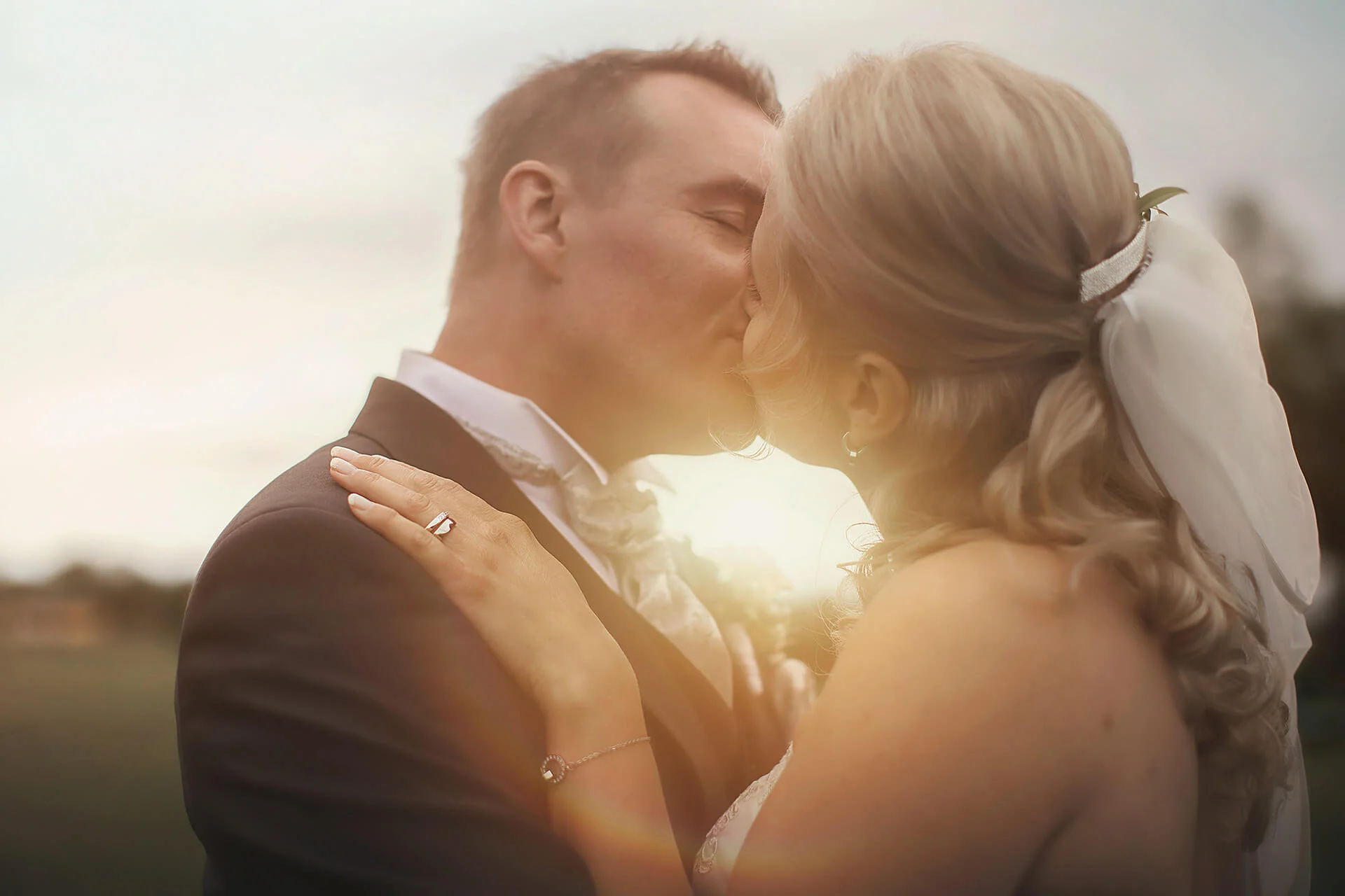 Bröllopsfotografering - porträtt brudpar som kysser varandra med solen bakom dom. Wedding photography - portrait bride and groom kissing each other with the sun behind them.