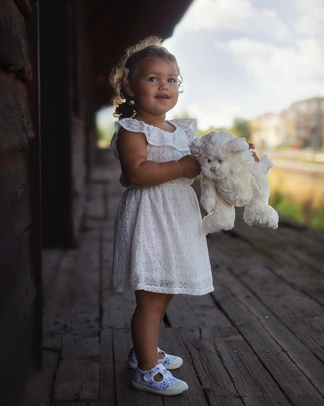 Barnfotografering - en glad liten flicka med lockigt brunt hår håller om sitt gosedjur. Barnfoto i Sala. Children's photography - a happy little girl with curly brown hair holds her stuffed animal.
