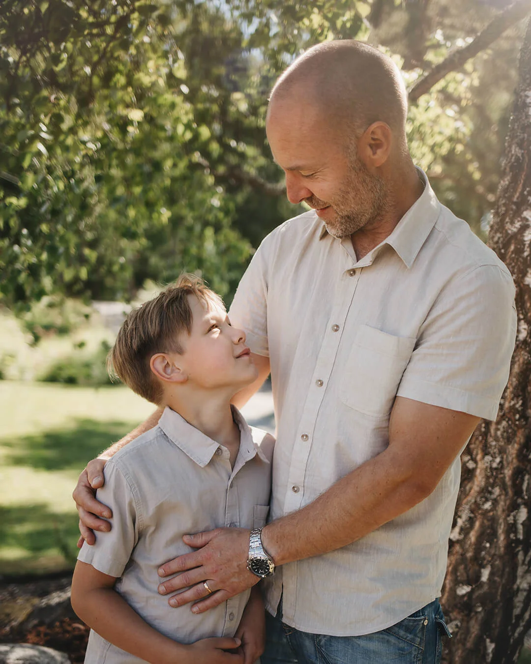 Familjefotografering - far och son porträtt. Pappan omfamnar sonen och dom tittar på varandra och ler. familjefoto i Sala. Family photography - father and son portrait. The father embraces the son and they look at each other and smile.